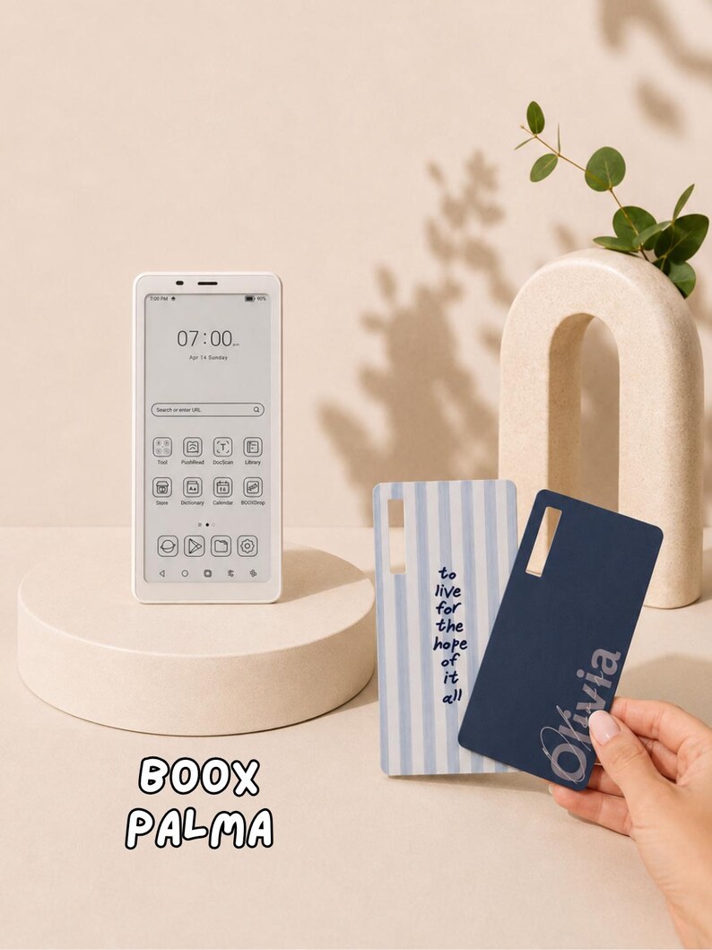 May include: A white Boox Palma e-reader displaying a digital interface with the time 07:00, alongside two rectangular protective cases: one with light blue vertical stripes and the text to live for the hope of it all, and one solid navy blue with the name Olivia.