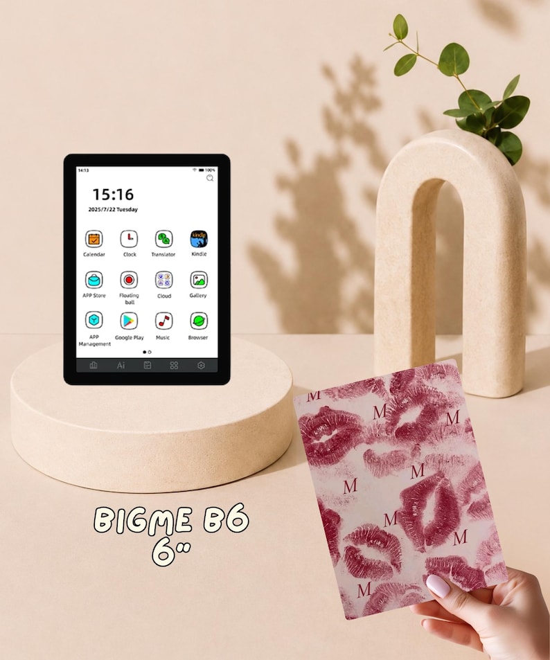 May include: A Bigme B6 6-inch e-reader with a black frame displaying a digital interface with app icons and time. Beside it is a rectangular cover featuring a repeating pattern of dark pink lipstick kiss marks and the letter M on a light background.