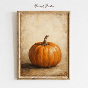 Op de afbeelding: Een ingelijste olieverfschilderijprint met een enkele oranje pompoen met een bruine steel, gecentreerd tegen een getextureerde, neutrale beige achtergrond. Het kunstwerk bevat bovenaan de tekst Berest Studio en zit in een lichte houten lijst.