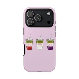 May include: A light pink phone case featuring a design of three iced matcha drinks with colorful layers and pink bows. Each drink has a straw. The phone case has a triple-lens camera.