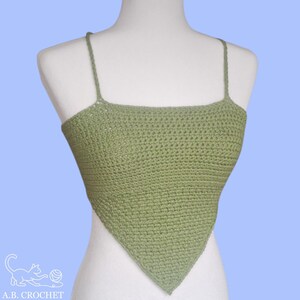 May include: A sage green crochet top with thin spaghetti straps. The top has a square neckline and a triangular shape. The item is displayed on a mannequin against a light blue background. The brand logo "A.B. CROCHET" is visible in the lower left corner.