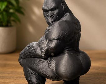 May include: A matte black figurine of a gorilla in a crouching pose, looking back over its shoulder. The sculpture features detailed fur texture on the arms and legs, a muscular build, and a smooth finish on the rounded posterior area.