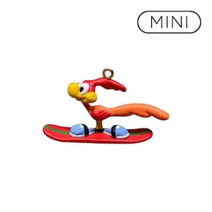 May include: A miniature ornament featuring a cartoon bird with a red head and orange tail, standing on a red snowboard with green stripes. The bird has large white eyes and blue feet. The word MINI is printed in black text inside a rounded rectangle.