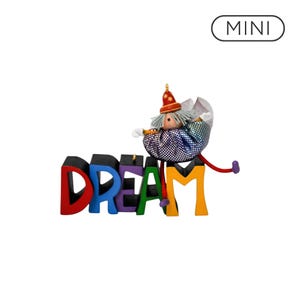 May include: A decorative ornament featuring the word DREAM in colorful block letters, with a small clown figure wearing a red hat and a shimmering, iridescent, multi-colored outfit sitting on top of the letter M. The text MINI is visible above.