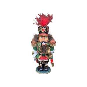 May include: A decorative nutcracker figure wearing a green and gold uniform with red accents. It features a tall black hat topped with red feathers, a dark brown faux fur beard, gold epaulets, and a sword at its side. The figure stands on a round base.