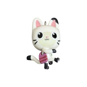 May include: A white cat figurine with large black eyes, pink inner ears, and a small pink nose. The cat has black markings on its ears and paws, and it is wearing a pink and red striped shoulder bag while in a dynamic walking pose.