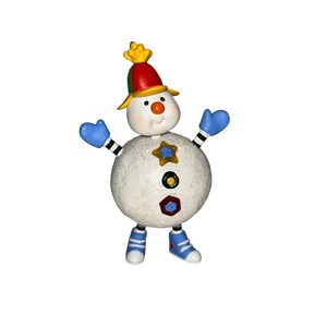 Puede incluir: Una figura de muñeco de nieve redonda, blanca y texturizada con un sombrero rojo, verde y amarillo. Tiene manoplas azules, brazos a rayas blancas y negras y zapatos azules. El cuerpo está decorado con una estrella amarilla y botones de colores.