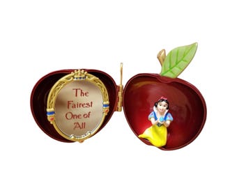 Peut inclure: Une boîte à bijoux articulée en forme de pomme avec un extérieur rouge brillant et une feuille verte. Le côté gauche présente un cadre de miroir doré avec le texte The Fairest One of All. Le côté droit contient une figurine en robe jaune.