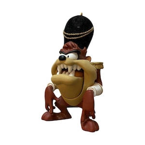 May include: A figurine of the Tasmanian Devil character wearing a tall black fuzzy hat with a gold cord trim. The figure has brown fur, a tan face, sharp white teeth, and is dressed in a red jacket with gold epaulets and white cuffs.