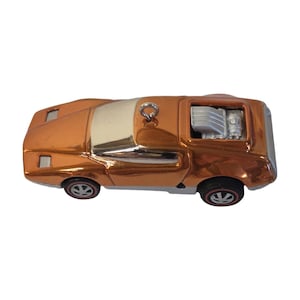 May include: A metallic copper-coloured toy car ornament featuring a silver-toned windscreen, a silver engine block exposed on the rear deck, and black wheels with red line detailing. A small metal eyelet is attached to the roof for hanging.