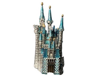 Peut inclure: Une figurine de château décorative présentant une structure argentée avec plusieurs tours surmontées de toits coniques bleu sarcelle. L'extérieur est orné de nombreuses petites pierres bleu clair et de détails dorés sur les flèches.
