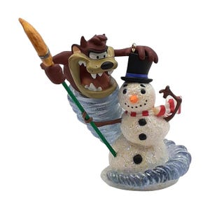 May include: A decorative figurine featuring the brown Tasmanian Devil character emerging from a translucent blue swirling tornado, holding a broom, positioned next to a white glittery snowman wearing a black top hat with a blue band and a red and white striped scarf.