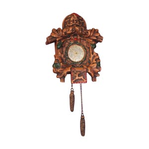 May include: A brown wall clock featuring a carved Santa Claus figure at the top, surrounded by oak leaves and green accents. The clock face is circular with gold hands, and a small square panel below depicts a reindeer. Two pinecone weights hang below.