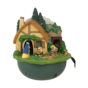 May include: A decorative figurine featuring a cottage with a thatched roof, a mine entrance labelled MINE, and several small figures including a person in a blue cape and yellow skirt, and multiple dwarves on a green base with a dark green bowl.