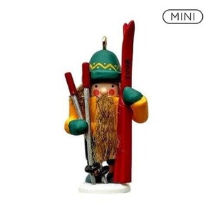 May include: A miniature wooden nutcracker figurine wearing a green hat and yellow jacket, featuring a long brown beard, holding two silver ski poles and a large red ski with the text 1908 printed on it, standing on a white circular base.