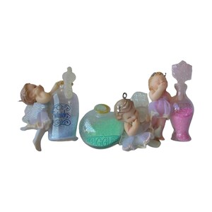 May include: Three small figurines of children with wings, each paired with a glass bottle. One bottle contains blue glitter and says Twinkles, another contains green glitter and says Giggles, and the third contains pink glitter with a star-shaped stopper.