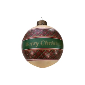 May include: A spherical Christmas bauble featuring a cream-coloured base with a central horizontal green band. The band displays the gold text Merry Christmas. Above and below the band are red sections with a dark green diamond grid pattern.
