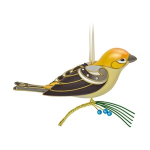 May include: A decorative bird ornament featuring a yellow head and chest with dark brown wings and tail feathers. The bird is perched on a gold-toned branch with green pine needles and small blue berries, suspended by a cream-colored ribbon.