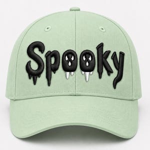Op de afbeelding: Een licht mintgroene baseballpet met het woord Spooky in het zwart op de voorkant geborduurd. De letters hebben een druipend effect en de twee o's zijn ontworpen als ogen met witte hoektanden die naar beneden hangen.