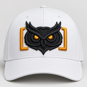 May include: A white baseball cap featuring a central embroidered design of a black owl face with piercing yellow eyes. The owl is flanked by two vertical orange brackets, one on each side, creating a framed look on the front of the cap.