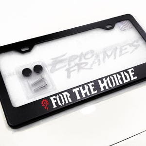 May include: Black license plate frame with the text "FOR THE HORDE" in white, and a red Horde symbol. The frame includes mounting hardware and the text "EPIC FRAMES".