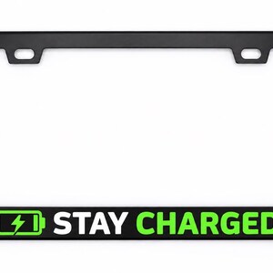 May include: A rectangular black number plate surround featuring a green battery icon with a lightning bolt symbol and the white text STAY CHARGED printed on the bottom horizontal bar. The frame includes two mounting holes at the top edge.