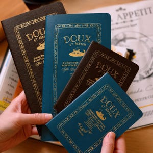 Peut inclure: Quatre carnets rectangulaires en brun foncé et bleu sarcelle avec des lettres dorées. Chaque couverture présente le texte "DOUX ET AÉRIEN" au-dessus d'une illustration de chat et d'une bordure décorative avec des couverts et ustensiles.