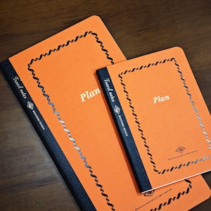 May include: Two orange notebooks with black spines and textured covers. Each notebook features a decorative black border, the word Plan in white, and the text Travel notes and BENSTORE DESIGN printed on the spine in white lettering.