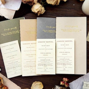 Könnte beinhalten: Vier rechteckige Notizbücher in Olivgrün, Beige, Grau und Creme mit goldfarbenem Folientext, der Live for yourself lautet. Jedes Notizbuch ist mit einer cremefarbenen Karte kombiniert, die den gedruckten Titel Domestic Midwife; or the best means of preventing danger in child-birth, considered, by Margaret Stephen, 1795 trägt.