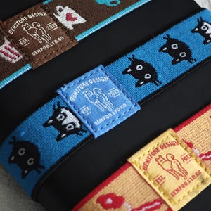 May include: Three elastic bands featuring woven patterns and rectangular fabric labels. The labels display the text BENSTORE DESIGN EST. 2013 SENPOD.LTD.CO with a graphic of two figures. The bands are brown, blue, and yellow with various icons.