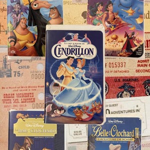 Könnte beinhalten: Eine Sammlung von fünf Walt Disney VHS-Kassetten mit den Animationsfilmen Un Empereur Nouveau Genre, Aladdin, Cendrillon, La Belle et le Clochard und La Belle et le Clochard II, die jeweils farbenfrohe Charakterillustrationen zeigen.