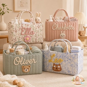 Op de afbeelding: Vier gewatteerde babybaskets met handvatten, elk gepersonaliseerd met een naam. De manden zijn gevuld met babybenodigdheden. Bloemen-, roze-, blauwe en groene ontwerpen met geborduurde details.
