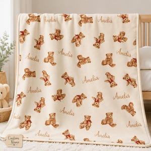 Puede incluir: Manta de bebé color crema con un patrón repetido de ositos de peluche marrones con bufandas rojas y el nombre "Amelia" en escritura marrón. La manta está hecha de material suave y es adecuada para una cuna o cochecito. Las palabras "Custom Name" están en una etiqueta.