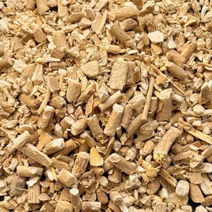 May include: A close-up shot of a pile of chopped, dried, tan-coloured roots and stems. The pieces vary in size and shape, with some appearing cylindrical and others more irregular. The texture is rough and fibrous, suggesting a natural product.