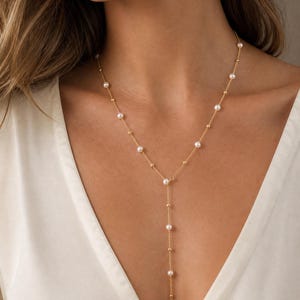 May include: A gold chain necklace featuring a Y-shaped drop design, accented with evenly spaced small white pearls and tiny gold beads along the entire length of the delicate metal chain, creating a layered appearance against the neckline.