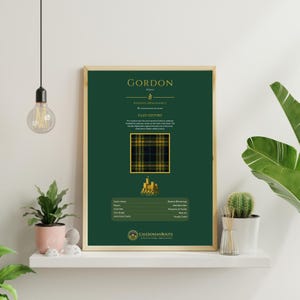 May include: A framed print with the name "GORDON" in gold, set on a dark green background. It features a tartan pattern and clan history information. The frame is a light wood colour.