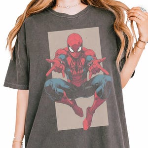 Pu&ograve; includere: Una t-shirt a maniche corte color grigio antracite con una stampa grafica del supereroe Spider-Man in posa accovacciata con le mani tese in avanti. Il personaggio &egrave; raffigurato in rosso e blu su uno sfondo rettangolare color beige.