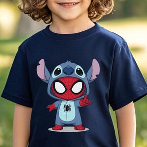 May include: A navy blue short-sleeved t-shirt featuring a graphic print of a character wearing a blue alien costume with large ears and a red and blue spider-themed mask. The character has a black spider emblem on its chest and is making a hand gesture.