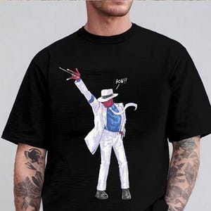 May include: A black short-sleeved t-shirt featuring a graphic print of a red-skinned character wearing a white fedora, a white suit jacket, a blue shirt, and white trousers. The character is in a dance pose with the text AOW!! printed nearby.