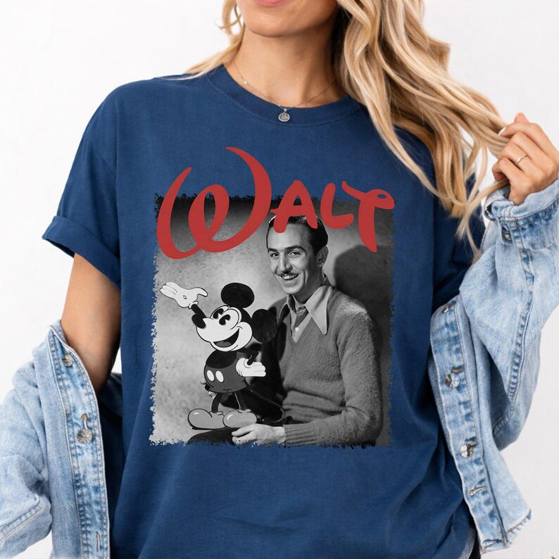 May include: Navy blue t-shirt with a black and white image of Walt Disney and Mickey Mouse. The word "Walt" is printed in red above the image. The shirt has short sleeves and a crew neck.