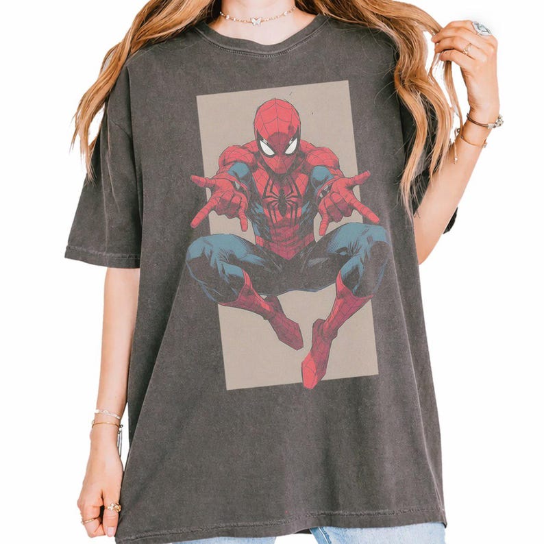 Pu&ograve; includere: Una t-shirt a maniche corte color grigio antracite con una stampa grafica del supereroe Spider-Man in posa accovacciata con le mani tese in avanti. Il personaggio &egrave; raffigurato in rosso e blu su uno sfondo rettangolare color beige.