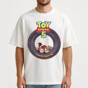 May include: A white short-sleeve t-shirt featuring a graphic of a black tire. Inside the tire are characters Woody, Jessie, and Buzz Lightyear. Above the tire is the text Toy Story 5, and below the tire is the text I knew it, I Knew You.