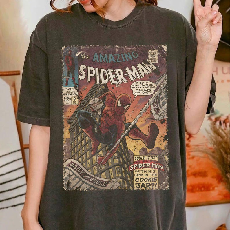 May include: Dark gray t-shirt featuring a vintage comic book cover of Spider-Man. The comic art shows Spider-Man swinging from a web, with text that reads "The Amazing Spider-Man" and "Daily Bugle."