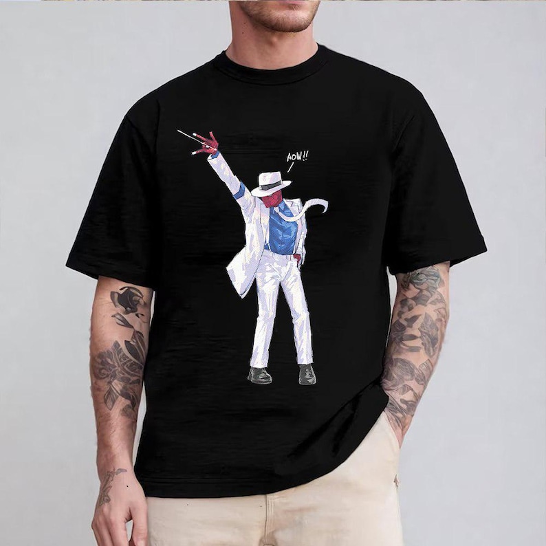 May include: A black short-sleeved t-shirt featuring a graphic print of a red-skinned character wearing a white fedora, a white suit jacket, a blue shirt, and white trousers. The character is in a dance pose with the text AOW!! printed nearby.