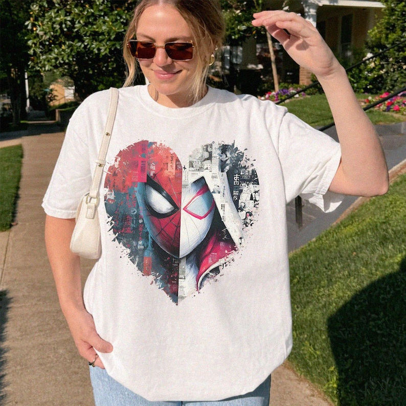 May include: A white short-sleeve t-shirt featuring a large heart-shaped graphic on the chest. The graphic is split into two halves, showing a red and black Spider-Man mask on the left and a white and red Spider-Gwen mask on the right with comic book art.