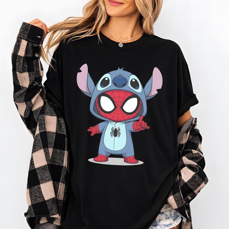May include: A black t-shirt featuring a graphic print of a blue alien character wearing a red and blue spider-themed costume with a spider emblem on the chest. The character has large white eyes, pointed ears, and is posed with one hand raised.