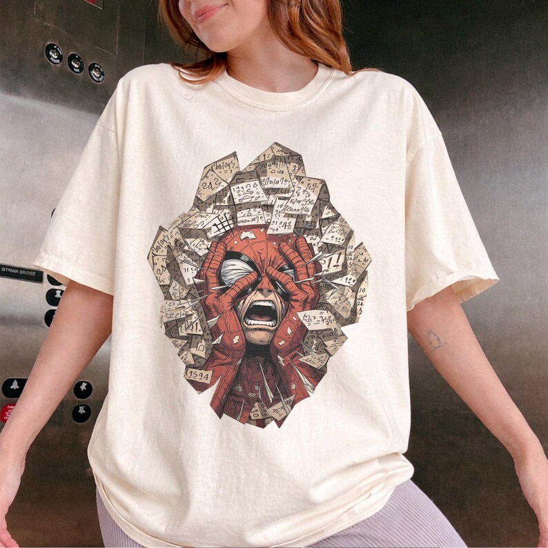 May include: A cream-colored short-sleeve t-shirt featuring a graphic print of a red masked character with hands pressed against their face in distress, surrounded by a cluster of floating, paper-like geometric shapes covered in handwritten numbers.
