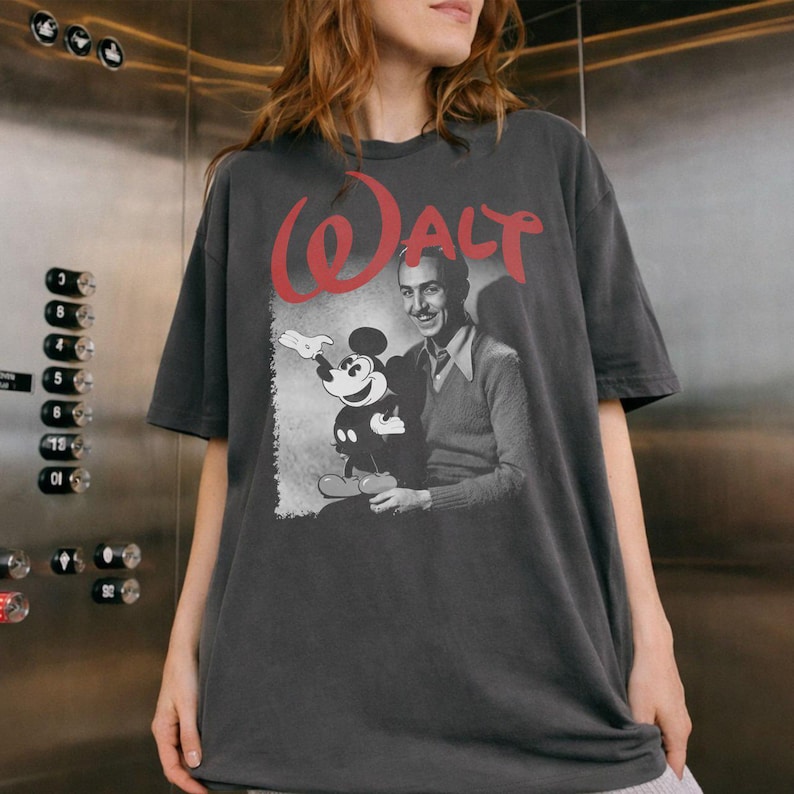May include: Dark grey t-shirt with a vintage graphic of Walt Disney and Mickey Mouse. The word "Walt" is printed in red above the image. The shirt has short sleeves and a relaxed fit.