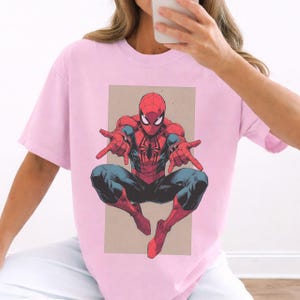 Pu&ograve; includere: Una t-shirt a maniche corte color rosa chiaro con una stampa grafica del personaggio dei fumetti Spider-Man in posa accovacciata con le braccia tese in avanti. Il personaggio &egrave; raffigurato in rosso e blu con un emblema a ragno nero.