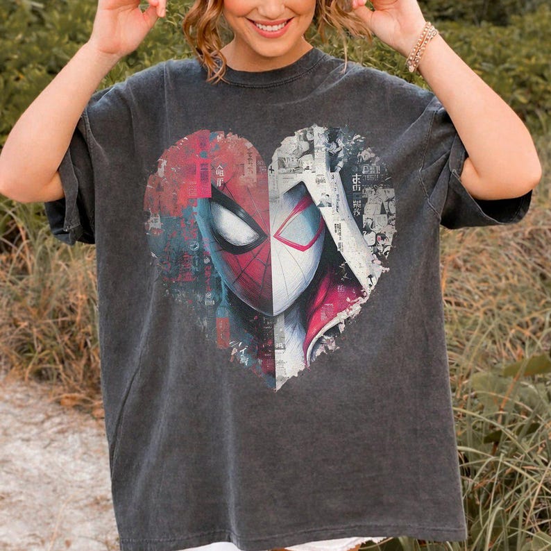 May include: A charcoal grey short-sleeve t-shirt featuring a large heart-shaped graphic on the chest. The graphic is split into two halves, showing a red and black Spider-Man mask on the left and a white and black Spider-Man mask on the right.